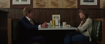 Movie still from “The Old Man & the Gun” (2018), directed by David Lowery – A man sitting at a table in front of two yellow candles; Medium shot, Over the shoulder angle