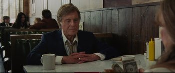 Movie still from “The Old Man & the Gun” (2018), directed by David Lowery – An older man sitting at a table in a restaurant; Medium shot, Over the shoulder angle