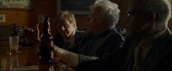 Movie still from “The Old Man & the Gun” (2018), directed by David Lowery – Two older men sitting at a table drinking beer; Medium shot, Over the shoulder angle