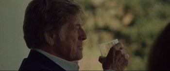Movie still from “The Old Man & the Gun” (2018), directed by David Lowery – An older man drinking from a plastic cup; Close Up shot, Over the shoulder angle