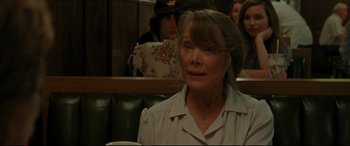 Movie still from “The Old Man & the Gun” (2018), directed by David Lowery – An older woman sitting at a table in front of a group of people; Close Up shot, Over the shoulder angle