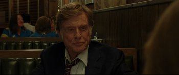 Movie still from “The Old Man & the Gun” (2018), directed by David Lowery – An older man wearing a suit and tie sitting at a table; Close Up shot, Over the shoulder angle