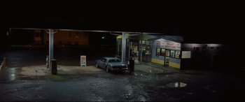 Movie still from “The Old Man & the Gun” (2018), directed by David Lowery – A car parked in front of a gas station at night; Extreme Wide shot, High angle