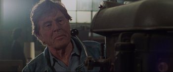 Movie still from “The Old Man & the Gun” (2018), directed by David Lowery – An older man in a denim shirt is working on a machine; Close Up shot, Low angle