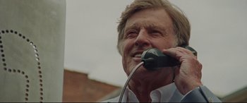 Movie still from “The Old Man & the Gun” (2018), directed by David Lowery – An older man talking on a phone while wearing a white shirt; Close Up shot, Low angle