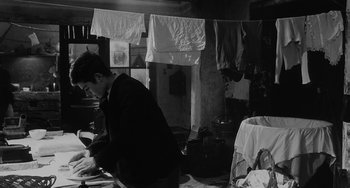 Movie still from “The Organizer” (1963), directed by Mario Monicelli – A man sitting on a table in front of a bunch of clothes; Medium shot, Over the shoulder angle