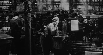 Movie still from “The Organizer” (1963), directed by Mario Monicelli – A man holding a wicker basket in a room filled with machines; Wide shot, High angle