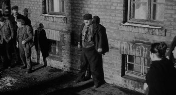 Movie still from “The Organizer” (1963), directed by Mario Monicelli – An older man standing in front of a brick building; Wide shot, Low angle