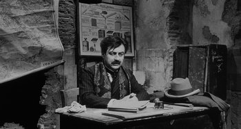 Movie still from “The Organizer” (1963), directed by Mario Monicelli – A man sitting at a table writing on a notebook; Medium shot, Low angle