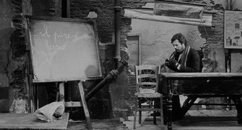 Movie still from “The Organizer” (1963), directed by Mario Monicelli – A man sitting at a table in front of an easel; Wide shot, High angle