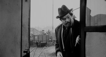 Movie still from “The Organizer” (1963), directed by Mario Monicelli – A man in a hat standing next to train tracks; Medium shot, Over the shoulder angle