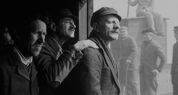Movie still from “The Organizer” (1963), directed by Mario Monicelli – Two men standing next to each other near a building; Medium shot, Low angle