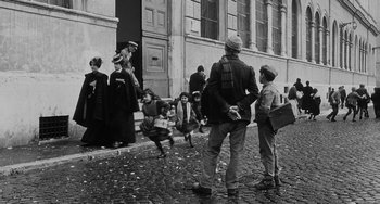 Movie still from “The Organizer” (1963), directed by Mario Monicelli – A group of people standing on a street; Wide shot, Over the shoulder angle