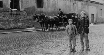 An old photo of a boy standing in front of a horse drawn carriage
