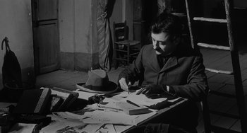 Movie still from “The Organizer” (1963), directed by Mario Monicelli – A black and white photo of a man sitting at a table with papers; Medium shot, High angle