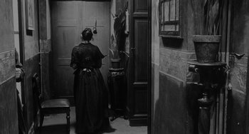 Movie still from “The Organizer” (1963), directed by Mario Monicelli – A woman in a black dress standing in front of an open door; Wide shot, Over the shoulder angle