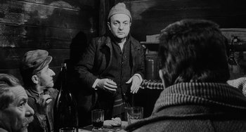 Movie still from “The Organizer” (1963), directed by Mario Monicelli – A man is sitting in front of a table with a drink; Medium shot, Over the shoulder angle