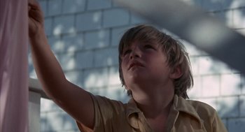 Movie still from “The Other” (1972), directed by Robert Mulligan – A young boy in a tan shirt is holding his arm up; Close Up shot, Low angle