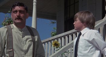 Movie still from “The Other” (1972), directed by Robert Mulligan – Two people standing on a porch with a sunflower; Medium shot, Low angle