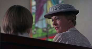 Movie still from “The Other” (1972), directed by Robert Mulligan – A woman wearing a hat sitting in front of a stained glass window; Close Up shot, Low angle