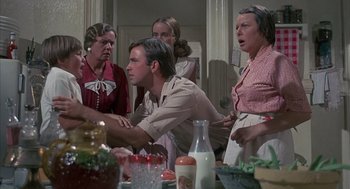 Movie still from “The Other” (1972), directed by Robert Mulligan – A group of people standing around a table; Medium shot, Over the shoulder angle