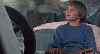 Movie still from “The Other” (1972), directed by Robert Mulligan – A young boy sitting on a chair in front of a tv; Medium shot, Low angle