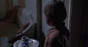 Movie still from “The Other” (1972), directed by Robert Mulligan – A boy sitting in front of a table with a cup of coffee; Medium shot, Over the shoulder angle
