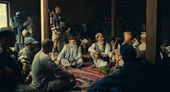 Movie still from “The Outpost” (2019), directed by Rod Lurie – A group of men sitting on the ground playing music; Wide shot, Over the shoulder angle