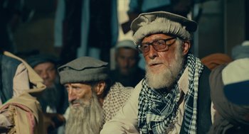 Movie still from “The Outpost” (2019), directed by Rod Lurie – A man with a beard wearing a hat and glasses; Close Up shot, Over the shoulder angle