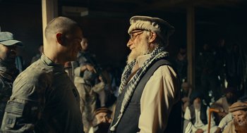Movie still from “The Outpost” (2019), directed by Rod Lurie – A man with a beard wearing a hat and a scarf; Medium shot, Over the shoulder angle