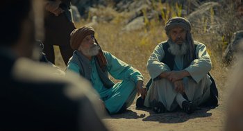 Movie still from “The Outpost” (2019), directed by Rod Lurie – Two older men sitting on the ground in a field; Wide shot, Over the shoulder angle