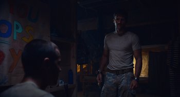 Movie still from “The Outpost” (2019), directed by Rod Lurie – A man standing next to another man in a dark room; Medium shot, Over the shoulder angle
