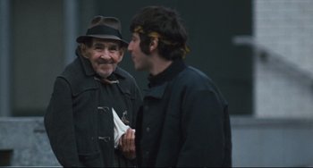 Movie still from “The Panic in Needle Park” (1971), directed by Jerry Schatzberg – A man wearing a hat and a jacket talking to another man; Medium shot, Over the shoulder angle