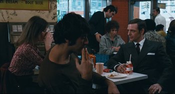 Movie still from “The Panic in Needle Park” (1971), directed by Jerry Schatzberg – A group of people sitting at a table eating food; Medium shot, Over the shoulder angle