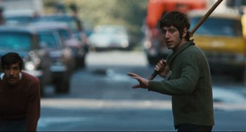 Movie still from “The Panic in Needle Park” (1971), directed by Jerry Schatzberg – A man holding a knife in the middle of a street; Medium shot, Over the shoulder angle