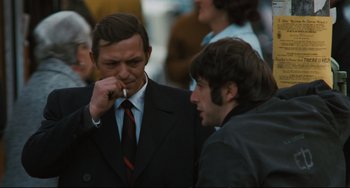 Movie still from “The Panic in Needle Park” (1971), directed by Jerry Schatzberg – A man in a suit smoking a cigarette next to another man in a suit; Medium shot, Over the shoulder angle