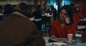 Movie still from “The Panic in Needle Park” (1971), directed by Jerry Schatzberg – A woman sitting at a table in front of a plate of food; Medium shot, Over the shoulder angle