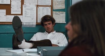 Movie still from “The Panic in Needle Park” (1971), directed by Jerry Schatzberg – A man sitting in front of another man in front of papers; Medium shot, Low angle