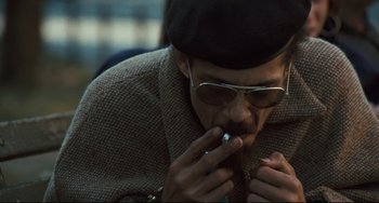 Movie still from “The Panic in Needle Park” (1971), directed by Jerry Schatzberg – A man in a hat and sunglasses is smoking a cigarette; Close Up shot, High angle