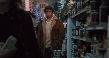 Movie still from “The Panic in Needle Park” (1971), directed by Jerry Schatzberg – A man standing in a grocery store looking at the camera; Medium shot, Over the shoulder angle