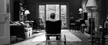 Movie still from “The Party” (2017), directed by Sally Potter – A man sitting in a chair holding a glass of wine; Wide shot, Low angle