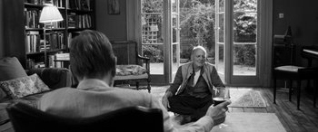 Movie still from “The Party” (2017), directed by Sally Potter – A man sitting on the ground in a living room; Medium shot, Over the shoulder angle