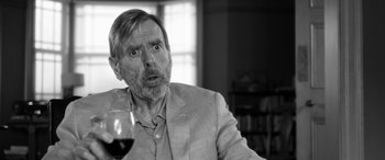 Movie still from “The Party” (2017), directed by Sally Potter – An older man is holding a glass of red wine; Close Up shot, Over the shoulder angle
