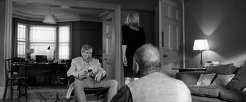 Movie still from “The Party” (2017), directed by Sally Potter – A man and a woman in a room with a man holding a camera; Medium shot, Over the shoulder angle