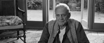 Movie still from “The Party” (2017), directed by Sally Potter – An older man sitting in front of an open door; Close Up shot, Low angle