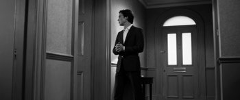 Movie still from “The Party” (2017), directed by Sally Potter – A man in a suit standing next to a door; Medium shot, Low angle