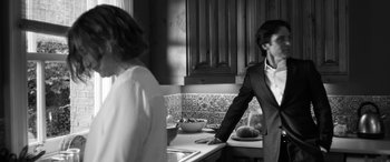 Movie still from “The Party” (2017), directed by Sally Potter – A man and a woman standing in a kitchen next to a sink; Medium shot, Over the shoulder angle