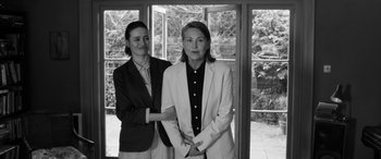 Movie still from “The Party” (2017), directed by Sally Potter – Two women standing next to each other in front of a window; Medium shot, Over the shoulder angle