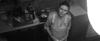 Movie still from “The Party” (2017), directed by Sally Potter – A woman standing in a kitchen holding a pan; Medium shot, High angle