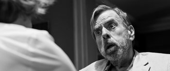 Movie still from “The Party” (2017), directed by Sally Potter – An older man looking at the camera with a surprised look on his face; Close Up shot, Over the shoulder angle